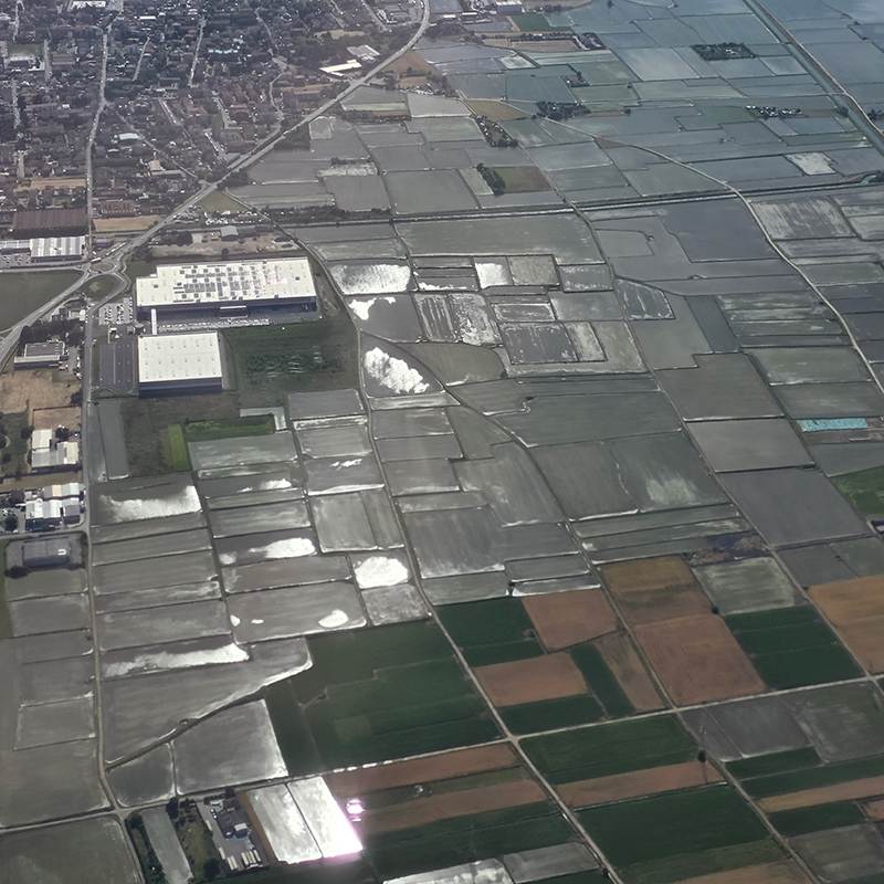 Aerial view of rectangular agricultural fields with irrigation ponds and a cluster of white-roofed buildings on the left.