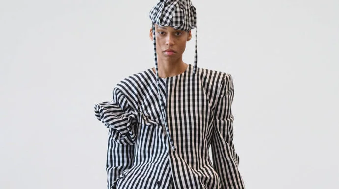 Model wearing a black-and-white gingham suit with oversized sleeves and a matching checkered cap, posed in a studio against a pale background.