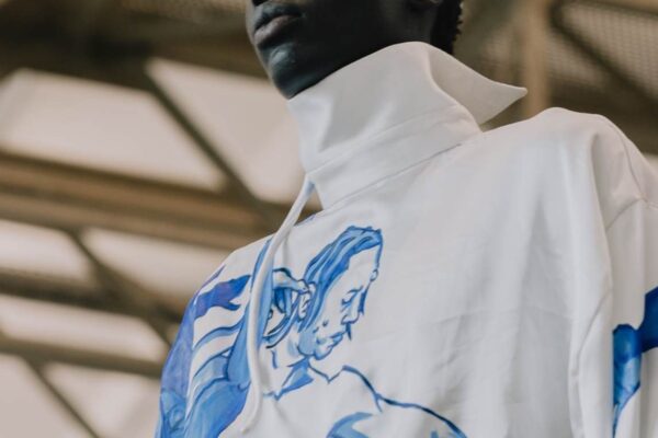 Back view of a person wearing a white shirt/jacket with a blue sketch design on the back, in an industrial indoor setting.