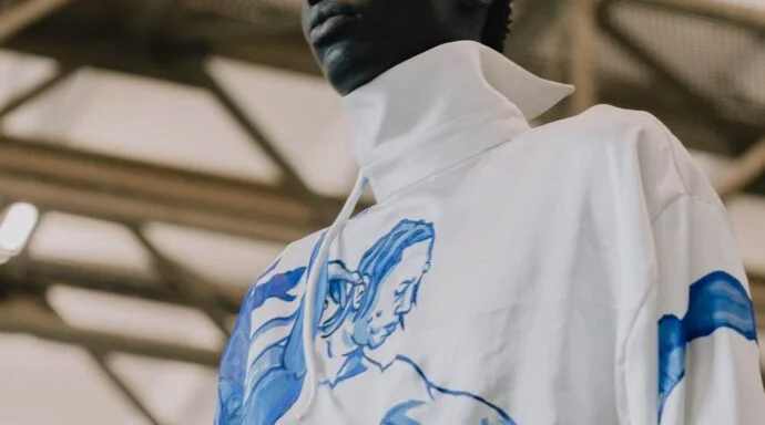 Back view of a person wearing a white shirt/jacket with a blue sketch design on the back, in an industrial indoor setting.